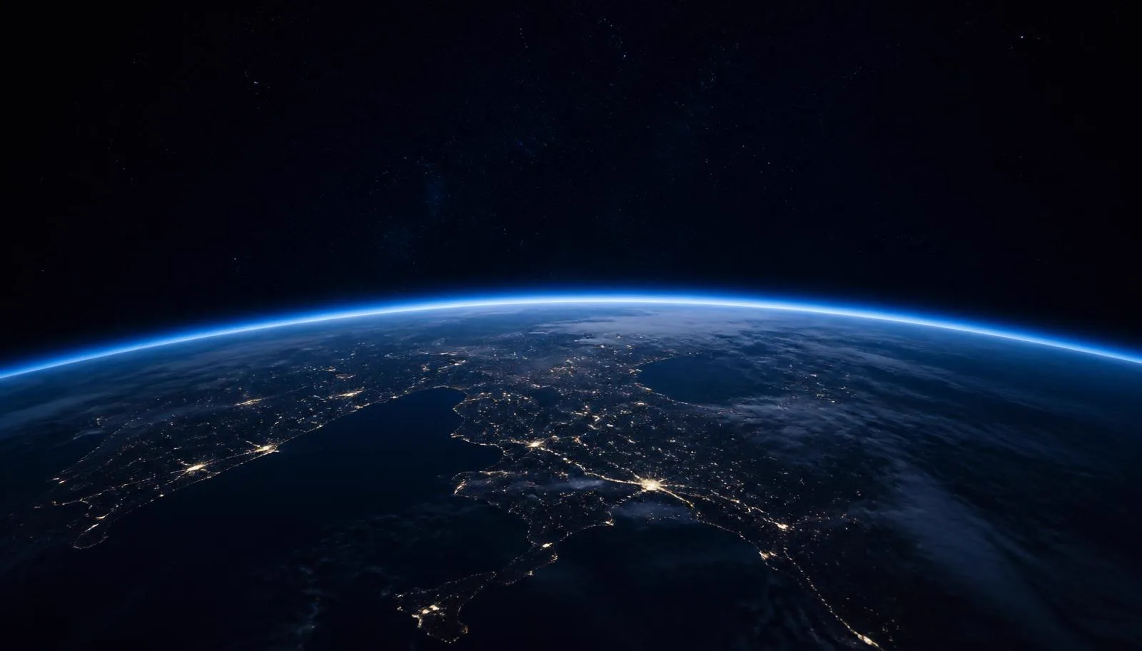 The curved limb of Earth at night with a thin blue atmospheric glow against space